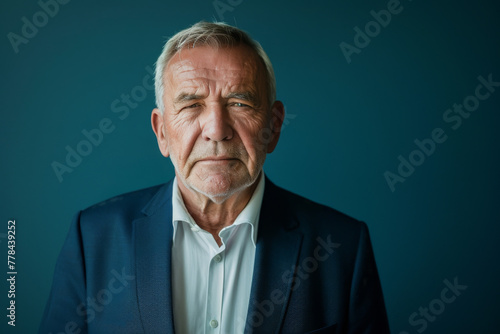 An older man in a suit and white shirt looks at the camera