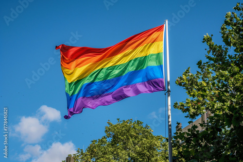A rainbow flag is flying in the sky. The flag is colorful and vibrant, representing the LGBTQ+ community. The blue sky in the background adds to the cheerful and uplifting mood of the image