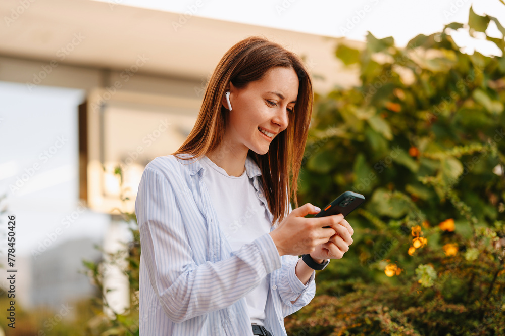 Outdoors shot of a young cheerful woman using her smart phone and ear buds in summer. Outdoors shot of a young cheerful woman using her smart phone and ear buds in summer.