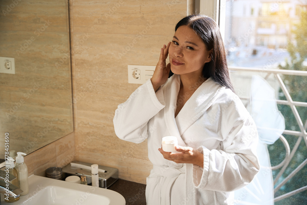 Pleased mature female is using her skincare product in morning Pleased mature female is using her skincare product in morning