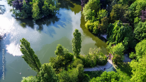 Amazing drone view on Park of Edmond de Rothschild. (stunning nature). weeping tree on shore and small bridge , distant person staying, pond shiny in afternoon sunbeams - fantastic Paris