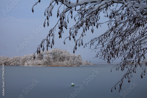 The beauty of a winter's day is on display in this image of Galve Lake in Trakai, Lithuania. The sun shines brightly overhead, casting a warm glow on the snow-covered landscape.