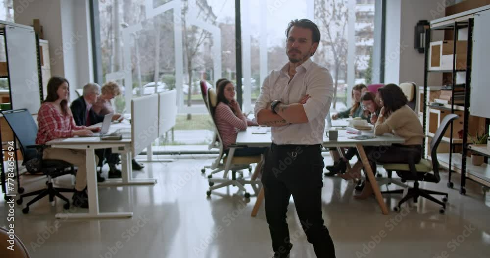 A young stylish businessman stands confidently in a contemporary office space as his colleagues focus on their work around him. A young stylish businessman stands confidently in a contemporary office space as his colleagues focus on their work around him.