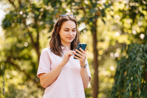 Close up shot of a young woman using her phone in park on a sunny day in summer.
