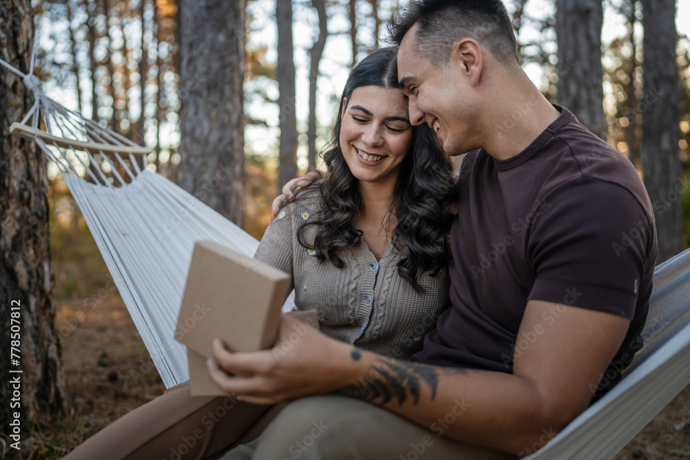 Young couple man and woman give present gift box while sit in nature Young couple man and woman give present gift box while sit in nature