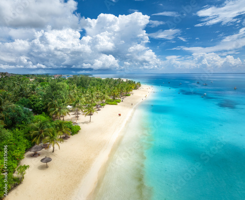 Aerial view of empty white sandy beach with palm trees, umbrellas, blue ocean, sky with clouds at sunset. Summer in Kendwa, Zanzibar island. Tropical landscape. Clear sea with azure water. Top view