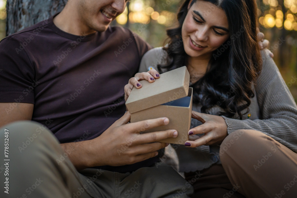 Young couple man and woman give present gift box while sit in nature Young couple man and woman give present gift box while sit in nature