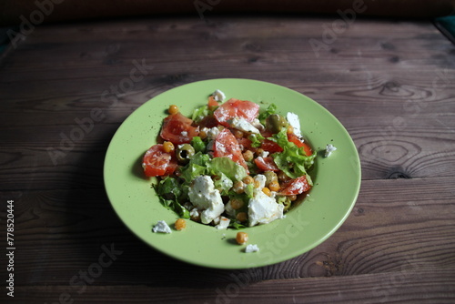 salad with vegetables, leaves, chickpeas, cheese in plate on wooden table