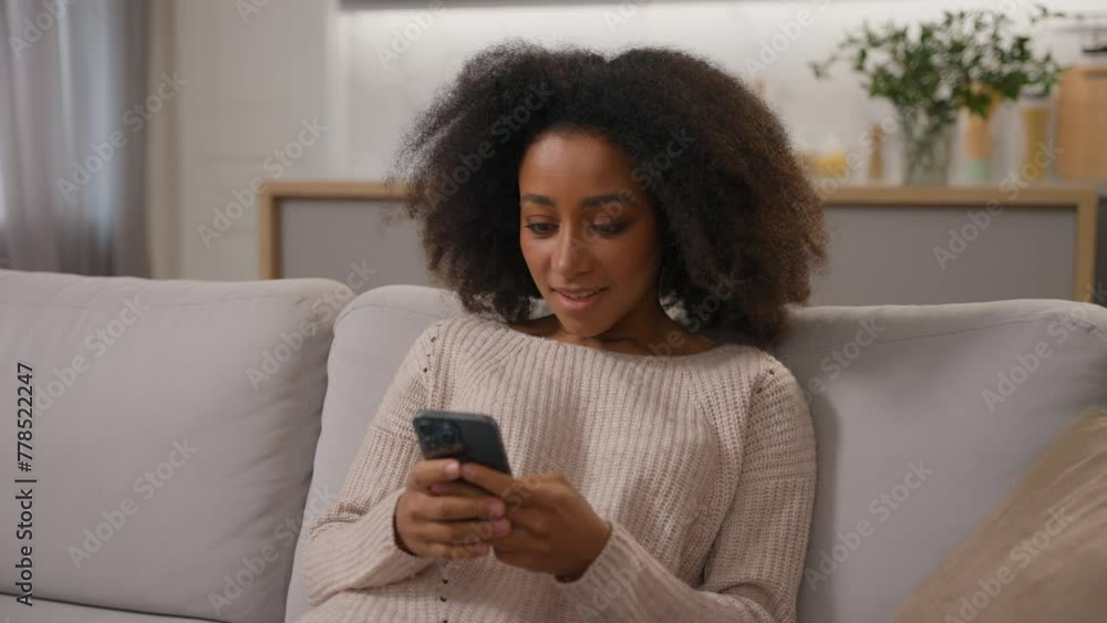 Happy African American girl smiling ethnic female woman using mobile phone cell gadget addicted chatting on smartphone shopping online on home sofa scrolling social media addiction influencer blogger Happy African American girl smiling ethnic female woman using mobile phone cell gadget addicted chatting on smartphone shopping online on home sofa scrolling social media addiction influencer blogger
