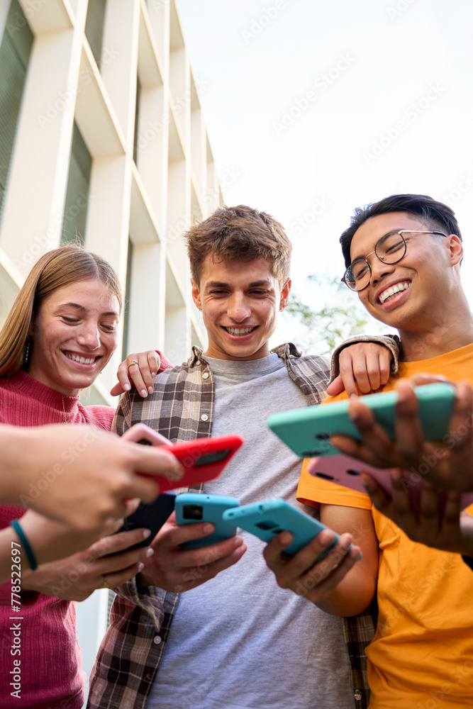 Obraz premium Vertical Group of multiracial generation z young smile cheerful people playing funny videos game on a smart phone in their hands. Friends having fun together using social on mobile cell outdoor