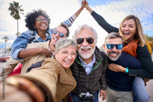 Photography Group diverse funny mature tourist friends posing piggyback with hands joined in air taking photo selfie together with front camera on travel outdoor