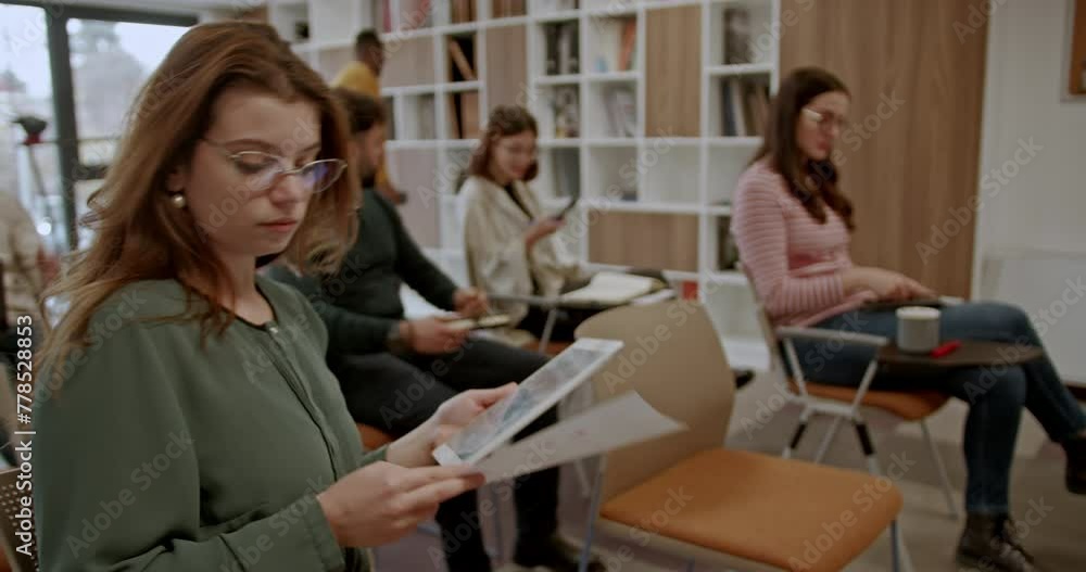 Attentively reading seminar materials, a businesswoman focuses while her colleagues engage in a modern office setting, showcasing her dedication and focus on professional development. Attentively reading seminar materials, a businesswoman focuses while her colleagues engage in a modern office setting, showcasing her dedication and focus on professional development.