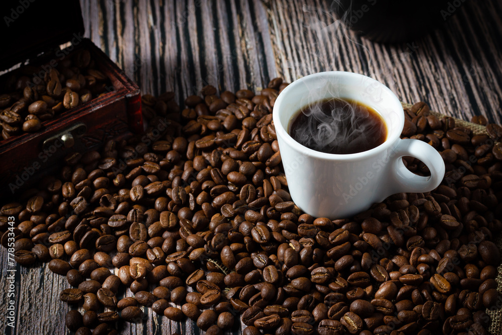 Naklejka premium A cup of coffee between selected roasted coffee beans on wooden background.