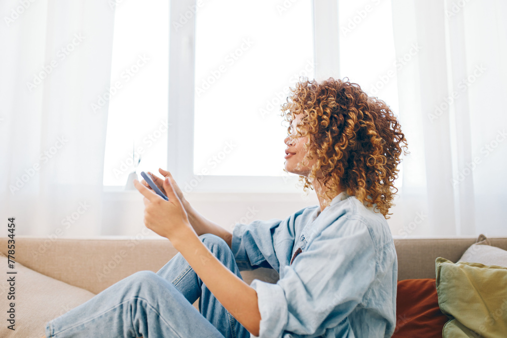 Smiling woman holding mobile phone while sitting on cozy sofa in a living room. Smiling woman holding mobile phone while sitting on cozy sofa in a living room.