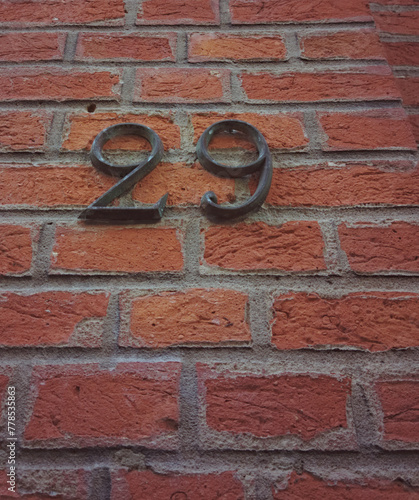 Metal covered with old black paint number twenty nine or 29. Brick in the background and surface as a texture