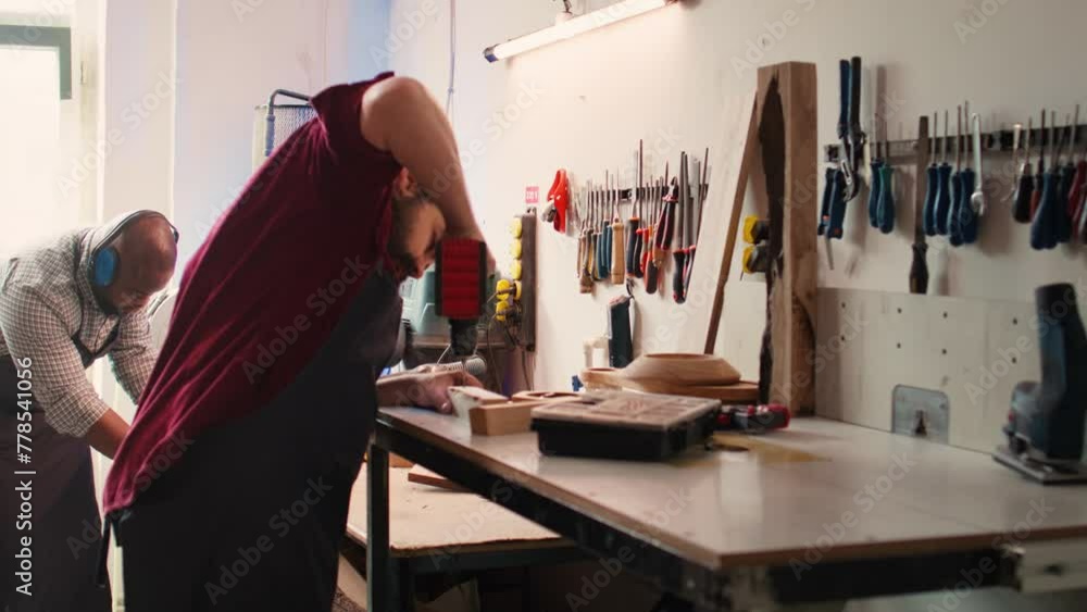 Woodworker in assembly shop using power drill to create holes for dowels in wooden board. Carpenter sinking screws into wooden surfaces with electric tool, doing precise drilling for seamless joinery Woodworker in assembly shop using power drill to create holes for dowels in wooden board. Carpenter sinking screws into wooden surfaces with electric tool, doing precise drilling for seamless joinery