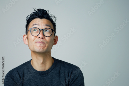 Decision, thinking and Asian man in studio with glasses, questions and brainstorming on grey background. Why, idea and male person with emoji, body language or choice gesture, puzzled or solution photo