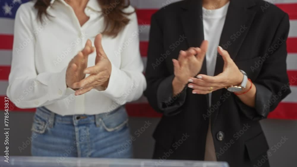 Two women in professional attire applauding indoors with the american flag in the background Two women in professional attire applauding indoors with the american flag in the background