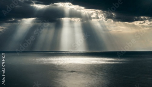Sunbeams break through storm clouds, illuminating a vast ocean in a dramatic seascape
