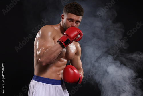 Man wearing boxing gloves in smoke on black background. Space for text