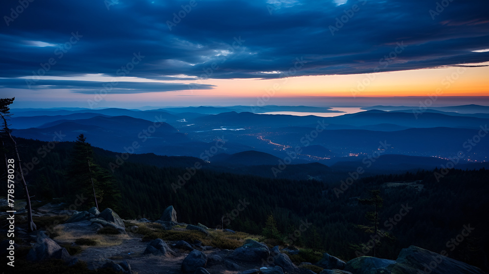 Twilight over a mountainous landscape with a glowing sunrise and scattered clouds in the sky.