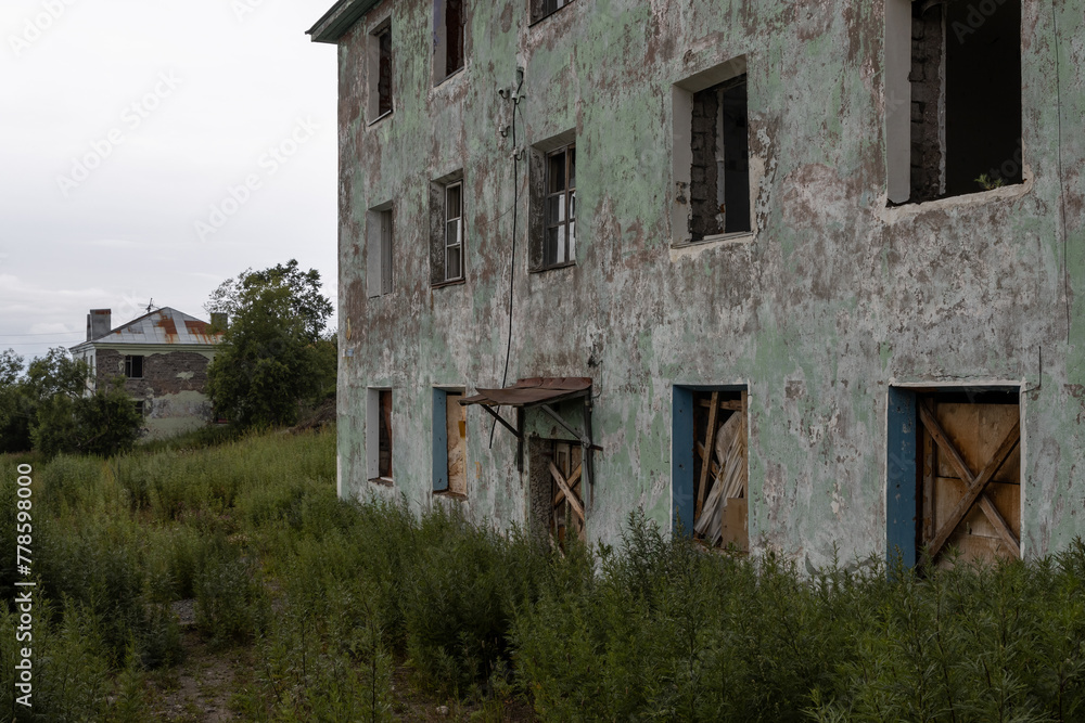 View of abandoned old houses in a provincial town. Broken and boarded up windows. Peeling cracked paint on the wall of a building. Overgrown city yard. Dilapidated buildings. View of abandoned old houses in a provincial town. Broken and boarded up windows. Peeling cracked paint on the wall of a building. Overgrown city yard. Dilapidated buildings.
