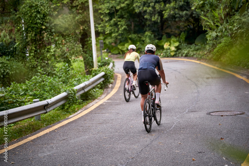 rear view of young asian couple cyclists riding bike outdoors on rural road