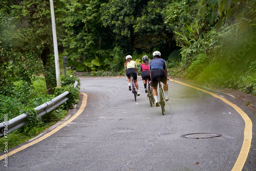 rear view of three young professional asian cyclists riding bike training outdoors on rural road