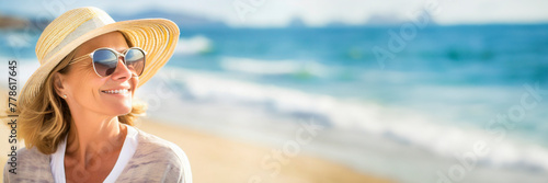 Happy mature woman relaxing on the beach wearing sunglasses and straw hat