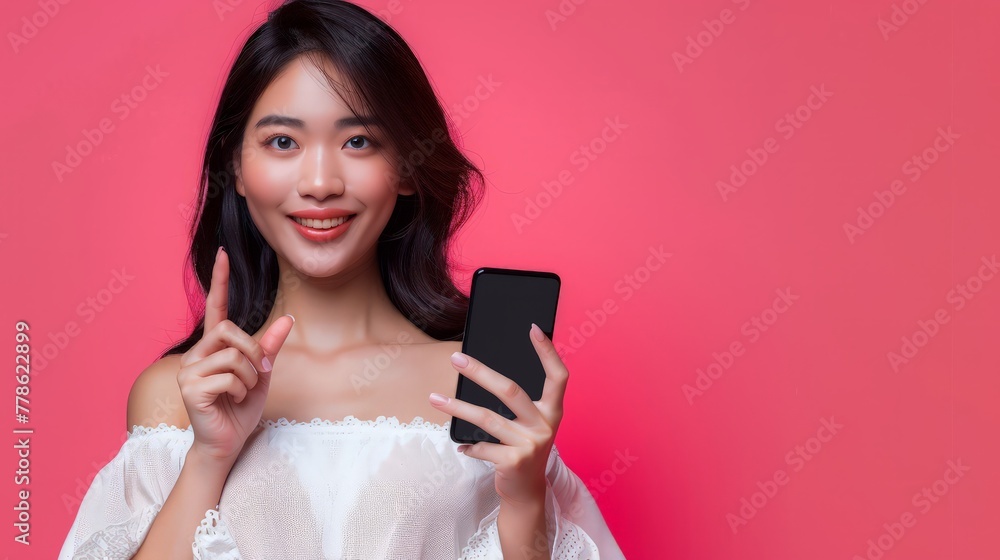 Attractive Young Asian woman pointing finger to mobile smartphone on isolated pink background. Attractive Young Asian woman pointing finger to mobile smartphone on isolated pink background.