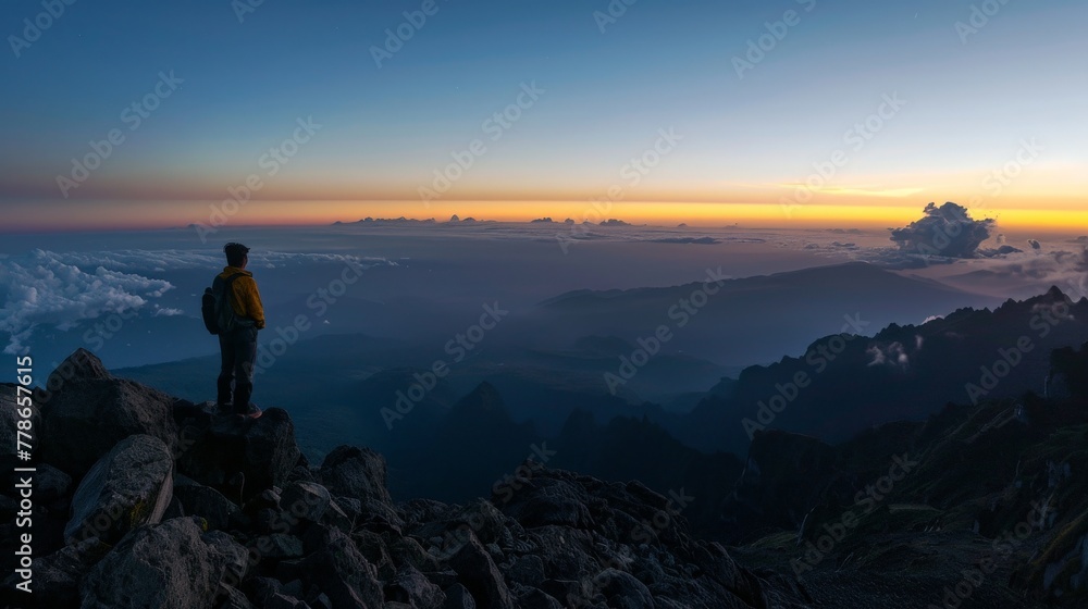 Solo traveler reaching the summit at dawn, embracing the serene beauty of a panoramic mountain view.
