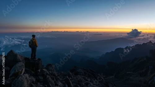 Solo traveler reaching the summit at dawn, embracing the serene beauty of a panoramic mountain view.