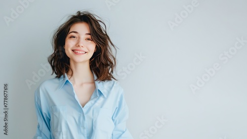 Confident Young Woman in Light Blue Shirt Smiling Against a Plain Background