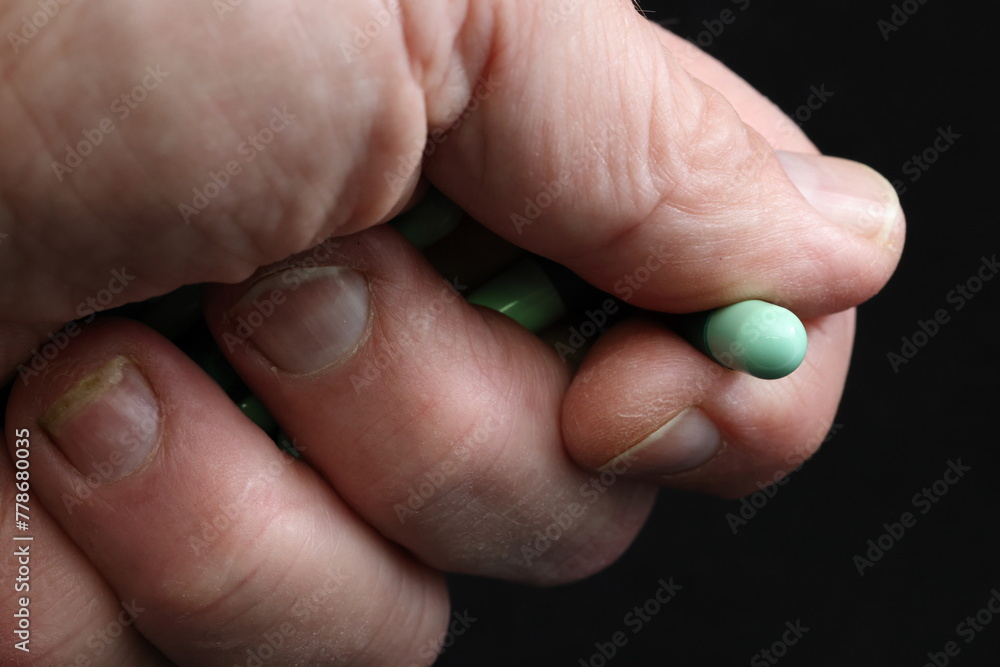 Prescription medicine (drugs) misuse, abuse. Green capsules held in closed hand. One capsule clasped between thumb and index finger. Black background. Copy space. Prescription medicine (drugs) misuse, abuse. Green capsules held in closed hand. One capsule clasped between thumb and index finger. Black background. Copy space.