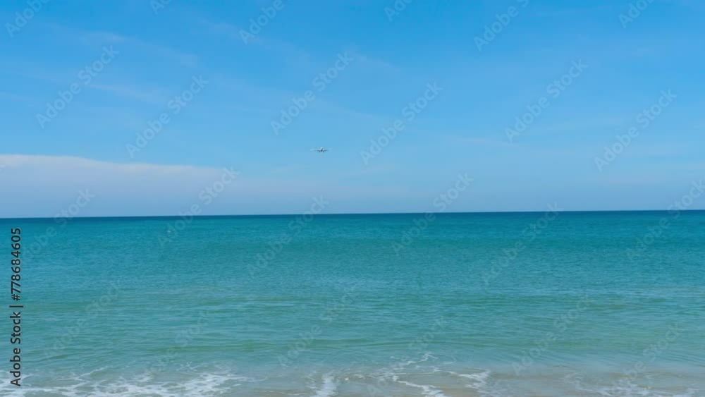 Azure sea waves crashing on the sandy beach of a tropical island. Long shot of a jet aircraft approaching descent landing. Airliner over the sea, ocean Azure sea waves crashing on the sandy beach of a tropical island. Long shot of a jet aircraft approaching descent landing. Airliner over the sea, ocean