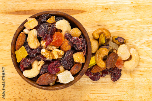 Top view of various dried mixed fruits and nuts in wooden bowl and pile on wooden board.