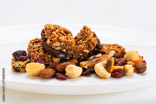 Closeup view of homemade peanuts, almond and chocolate mini protein bars on pile of mixed fruits and nuts on wooden board.