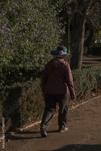Mujer anciana, paseando sola por el parque, gorra azul, vista de espaldas, demencia, vejez photo