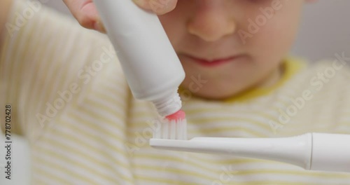 Child applying toothpaste on a toothbrush photo