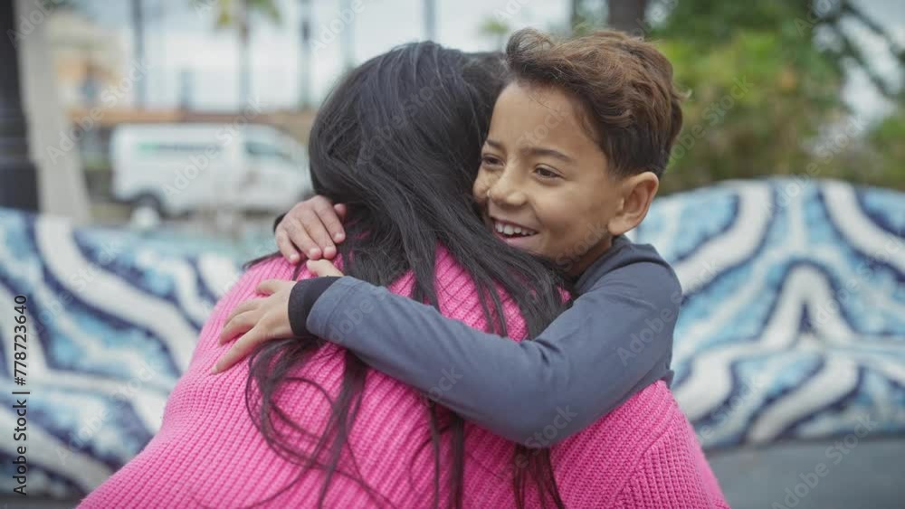 Mother and son embrace joyfully in an urban park, showcasing love and family bonds against a backdrop of greenery and street. Mother and son embrace joyfully in an urban park, showcasing love and family bonds against a backdrop of greenery and street.