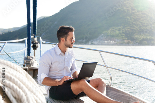 Man working on yacht office with laptop. Summer traveling on sailboat with insurance. Traveler using computer, Internet. Freelancer workplace in silence, social distance. Successful business lifestyle