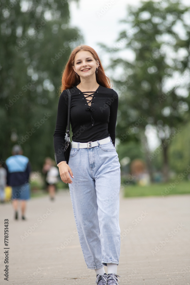 Portrait of a young beautiful red-haired girl in a summer park.