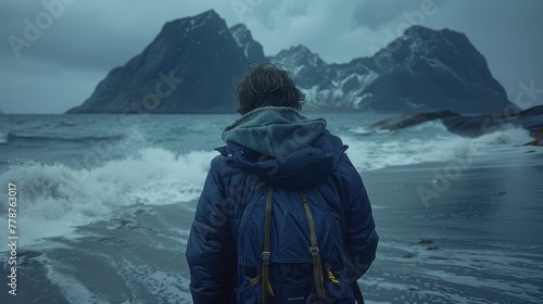 a man is far away, standing with his back against the backdrop of the huge mountains in Lofoten. cold colors