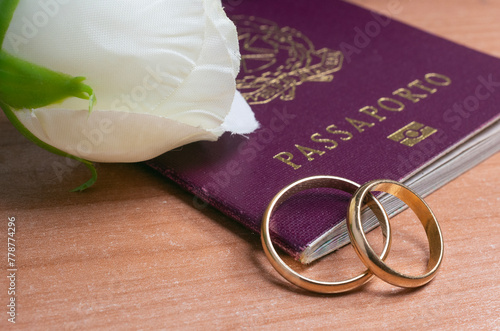 Gold wedding rings and a white rose resting on an Italian passport