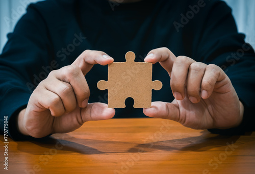 A jigsaw puzzle holding businessman's hand. Person hands showing empty piece of important jigsaw puzzle on wood table. Business solution and idea, partnership, elements of career success part concept.