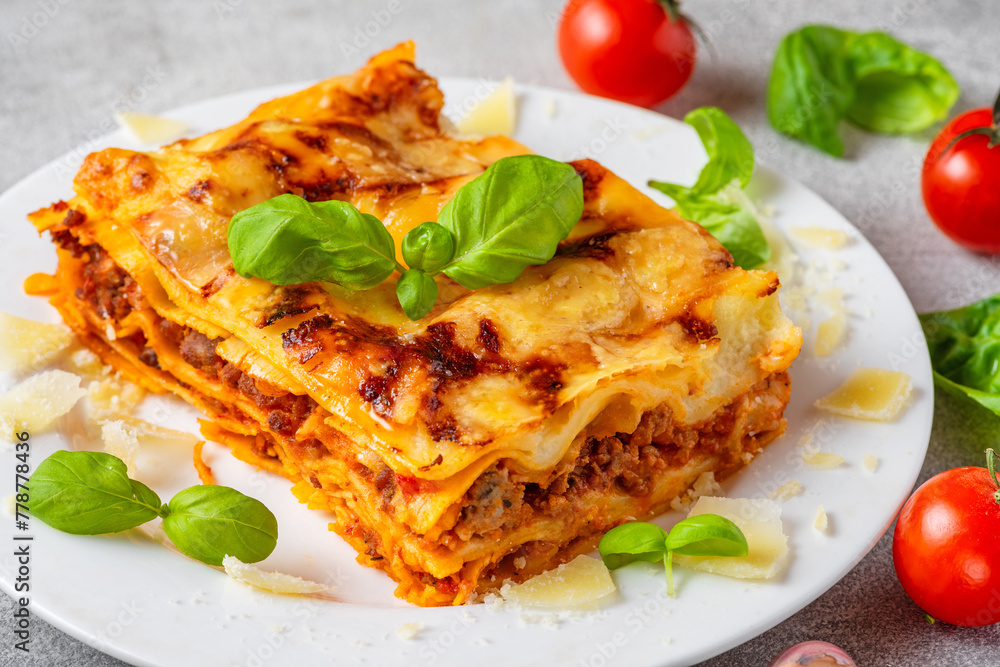Close up of meat lasagna with fresh basil, tomatoes and parmesan cheese in a plate. Italian cuisine. Delicious food for dinner