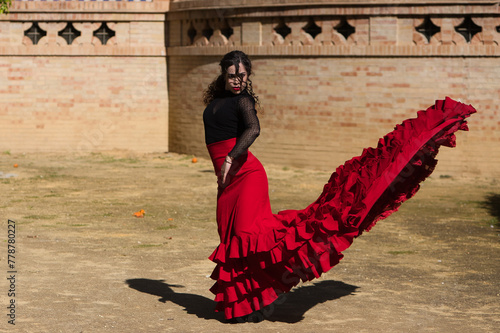 Beautiful woman dancing flamenco in Seville, Spain. She wears a red and black dress typical of a flamenco dancer with a lot of art, you can see the movement in the air of the frilly dress.
