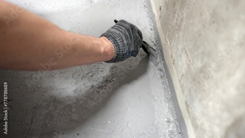 Brush with gray primer. A man paints the concrete floor in his bathroom with a gray brush. Waterproofing the floor in the bathroom. Paint the floor gray with a brush, close-up.
