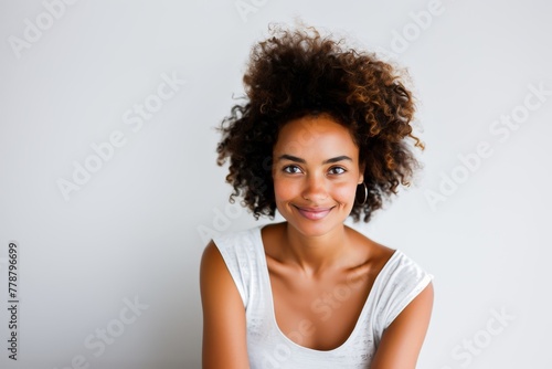 A radiant young woman with a beautiful curly hair, smiling joyfully against a white background.
