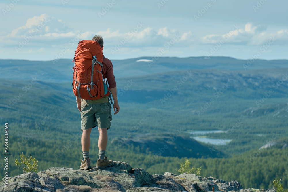 Man wearing a backpack standing on the peak of a mountain, looking out at the vast landscape below